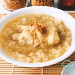 A hearty rice porridge in a bowl with juicy tender chicken pieces, combined with fragrant spices such as garlic, ginger and turmeric, topped with fried garlic