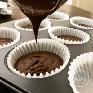 Dividing and pouring chocolate cupcake batter into each cupcake liner placed in a 12 cup muffin tin