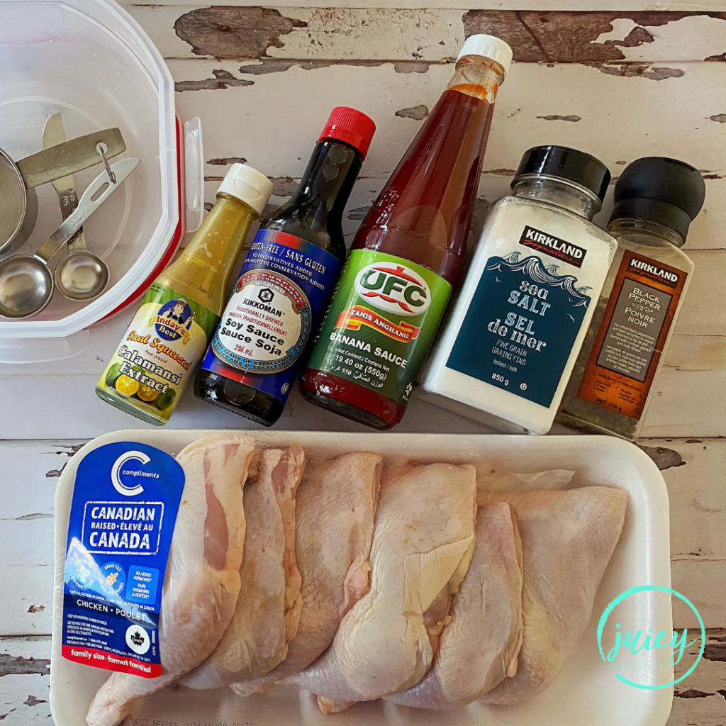 Ingredients for Filipino BBQ Chicken Recipe laid out on a white wooden table. Ingredients are 6 quarter chicken pieces, a small bottle of calamansi extract, bottle of gluten free soy sauce, bottle of banana ketchup, salt, pepper.