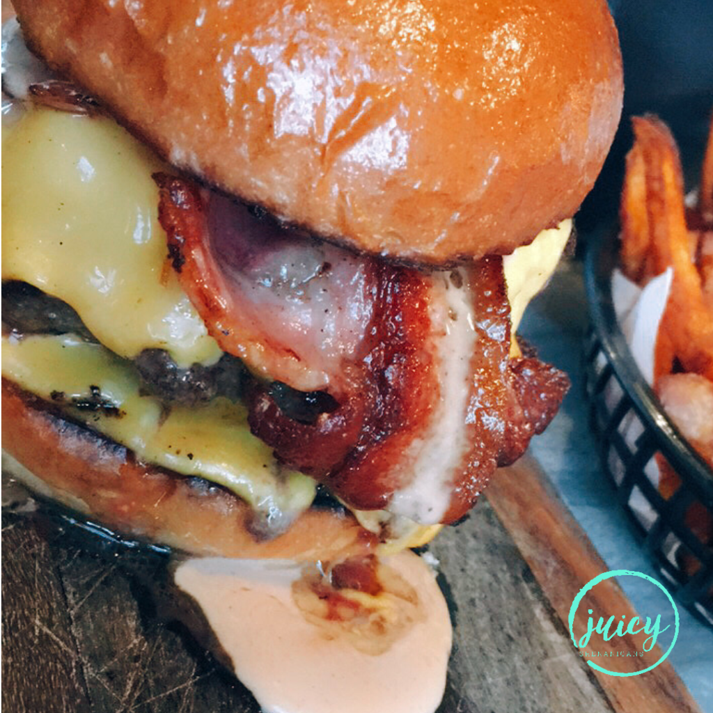 Close up for Burger Point's Big Boss Double Burger showing mouthwatering bacon and melting cheese on side with sauce dripping on the side