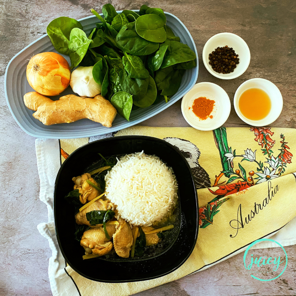 Top view of traditional Filipino Tinola served in a square black plate, with steamed jasmine rice. Ingredients used to create the dish are pictured in the background including ginger root, garlic, onion, spinach leaves, fish sauce, pepper and turmeric.