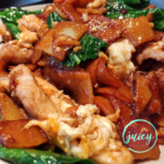 Close up image of Thai pad see ew, showing the flat rice noodles, chinese broccoli, chicken and eggs