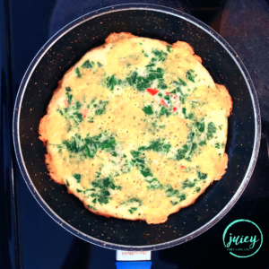 top view of spinach tomato omelette cooking in a pan