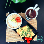 breakfast platter that includes spinach tomato omelette, cut into triangle pieces, garlic rice and fresh grape tomatoes, with hot tea in a mug.