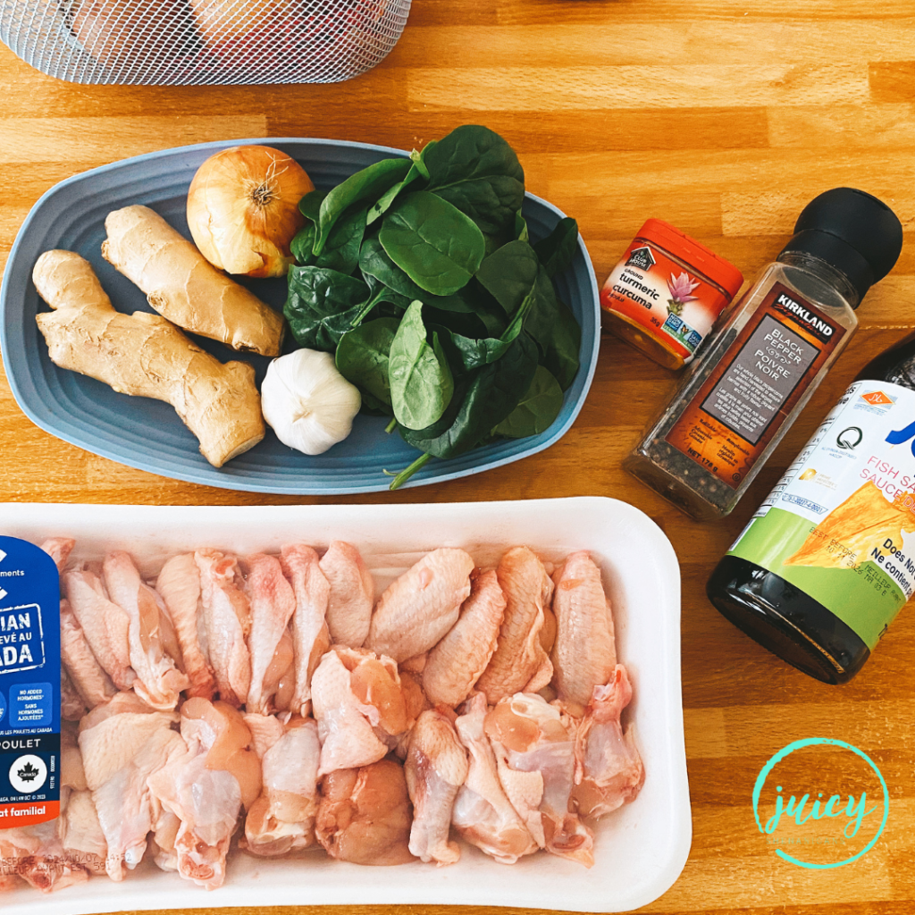 Ingredients for Filipino chicken tinola laid out on a bamboo counter top. Ingredients include chicken drumettes, ginger root, onion, garlic, spinach leaves, fish sauce, black pepper, turmeric.